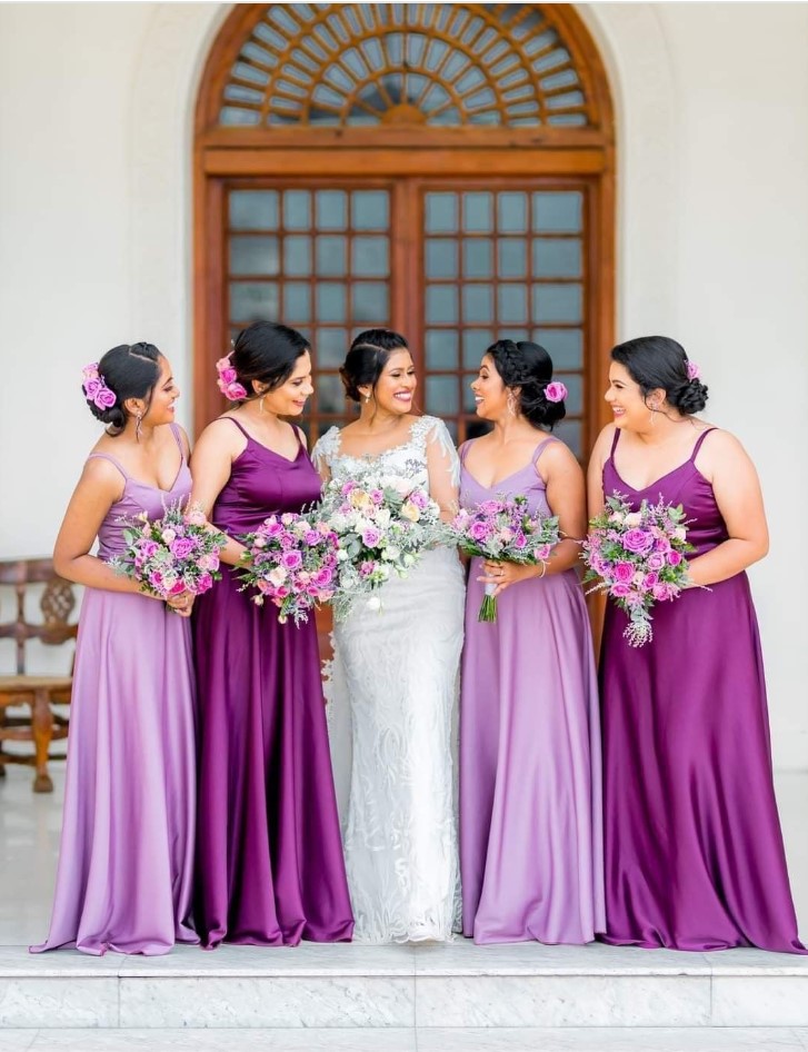 Bridesmaids in purple and lilac outfits together with the bride in her white gown. 
