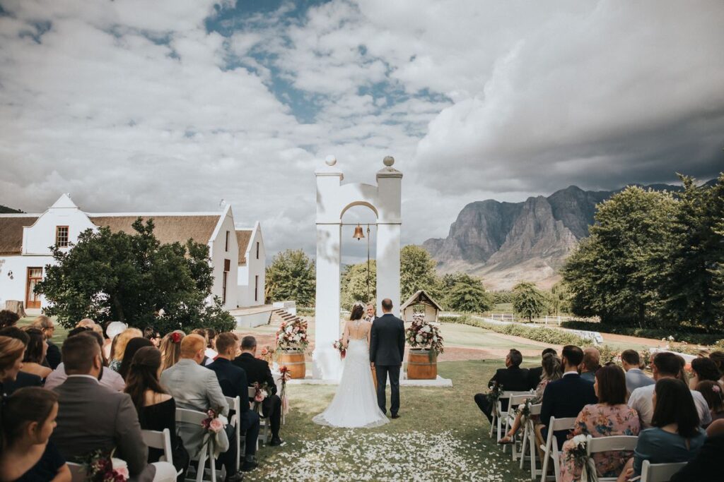 Zorgvliet Wine Estate bride and groom and people seated at an outdoor wedding. Image Source: whichwinefarm